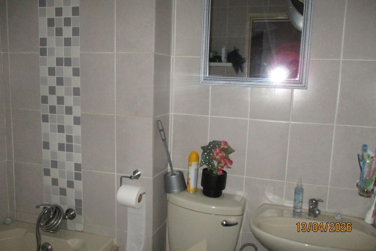 A functional bathroom featuring neutral wall tiles with a mosaic accent, a pedestal basin, and a bathtub with a shower mixer.