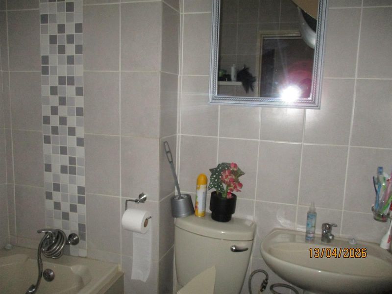 A functional bathroom featuring neutral wall tiles with a mosaic accent, a pedestal basin, and a bathtub with a shower mixer.