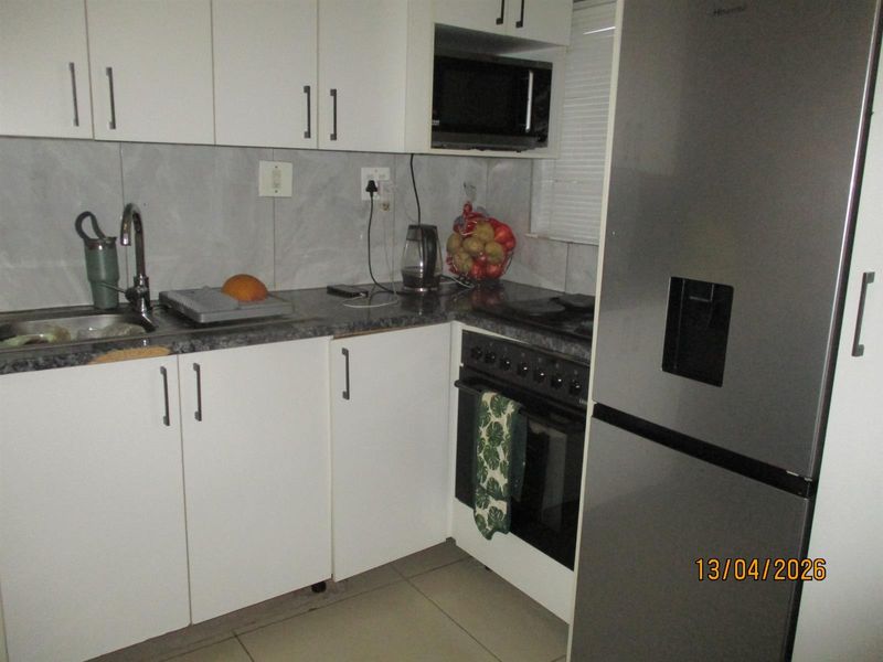 Compact kitchen featuring white cabinetry, dark laminate countertops, tiled backsplash, and integrated appliances including an oven, hob, and microwave.