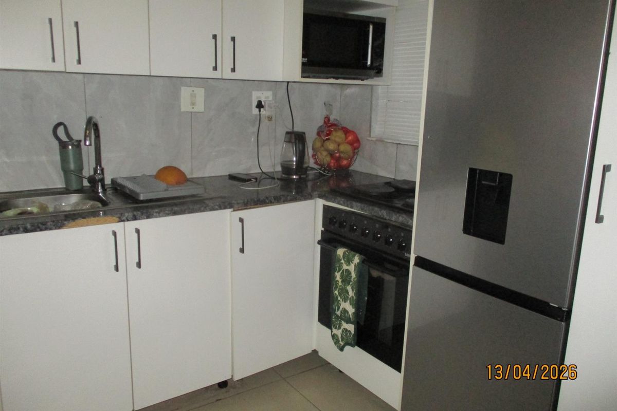 Compact kitchen featuring white cabinetry, dark laminate countertops, tiled backsplash, and integrated appliances including an oven, hob, and microwave.