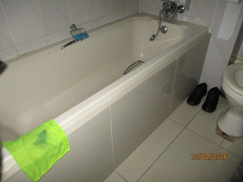 A dated bathroom featuring a standard bathtub with shower mixer, tiled walls, and floor tiles, requiring cosmetic updates to improve its overall condition.