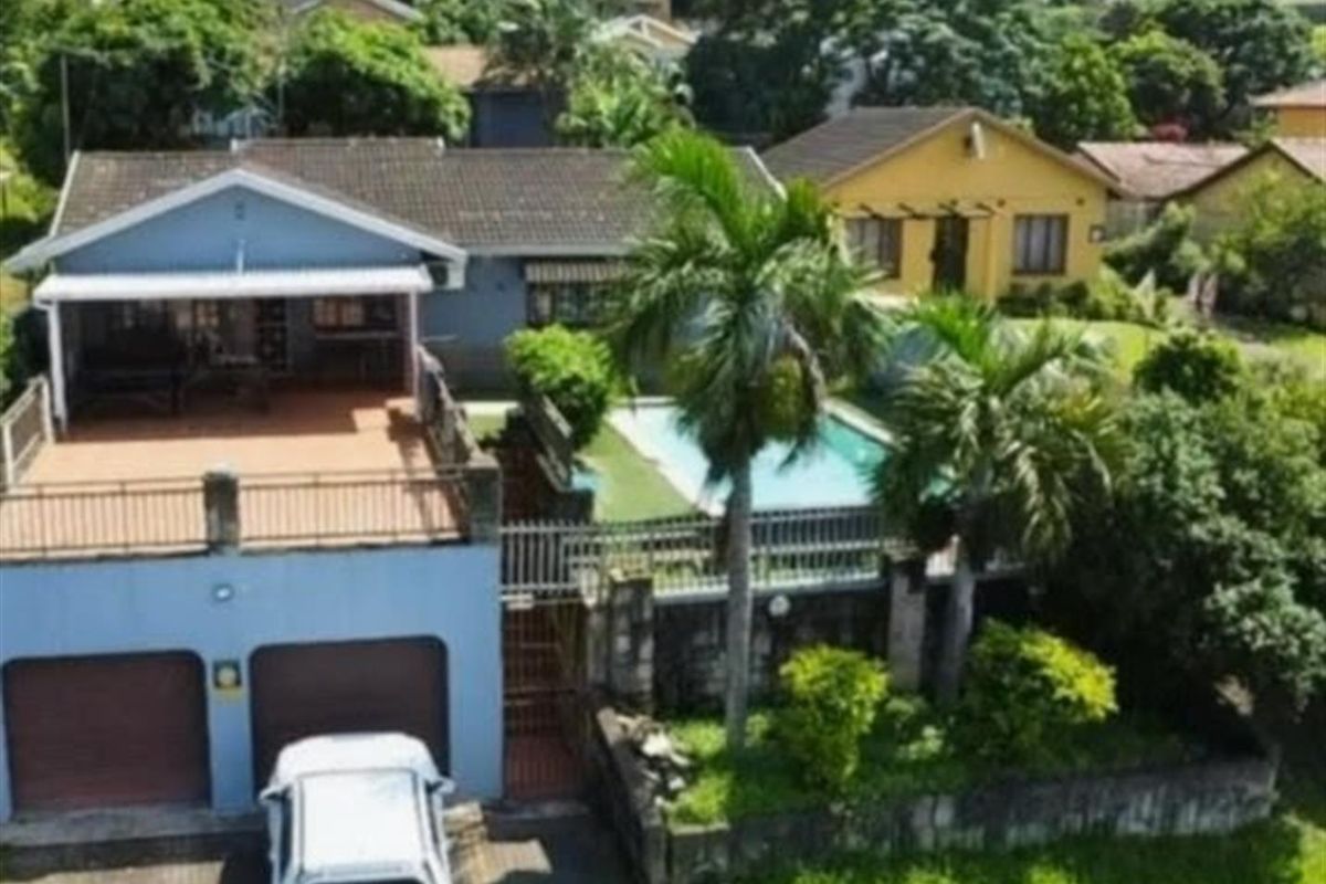 Aerial view of a residential property featuring a double garage, elevated patio, and a swimming pool set within a landscaped garden.