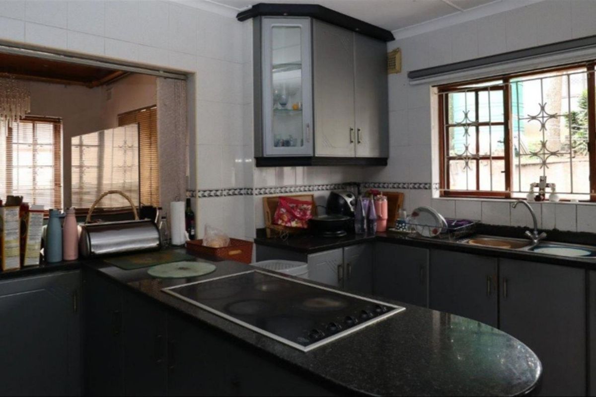 A functional kitchen featuring dark granite countertops, built-in hob, and grey cabinetry with a pass-through window to the adjacent living area.