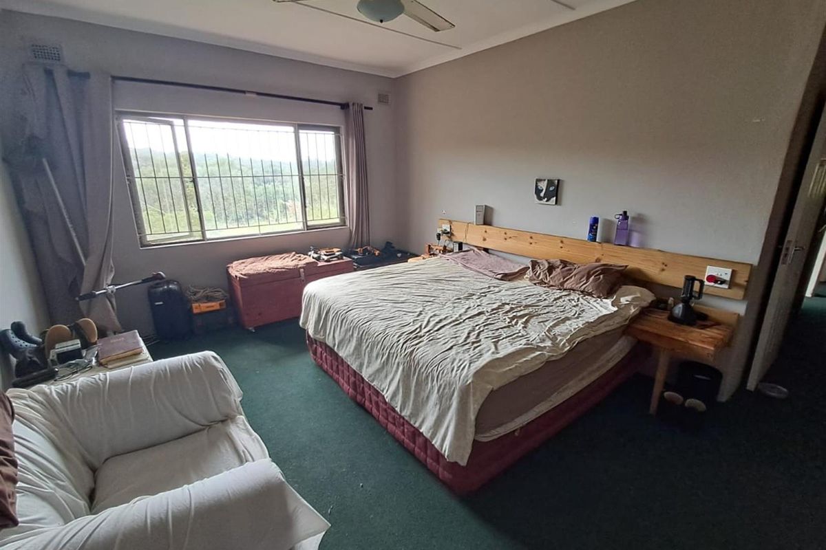 A spacious bedroom featuring large windows with security bars, a ceiling fan, and carpeted flooring, offering a functional layout with potential for modernization.