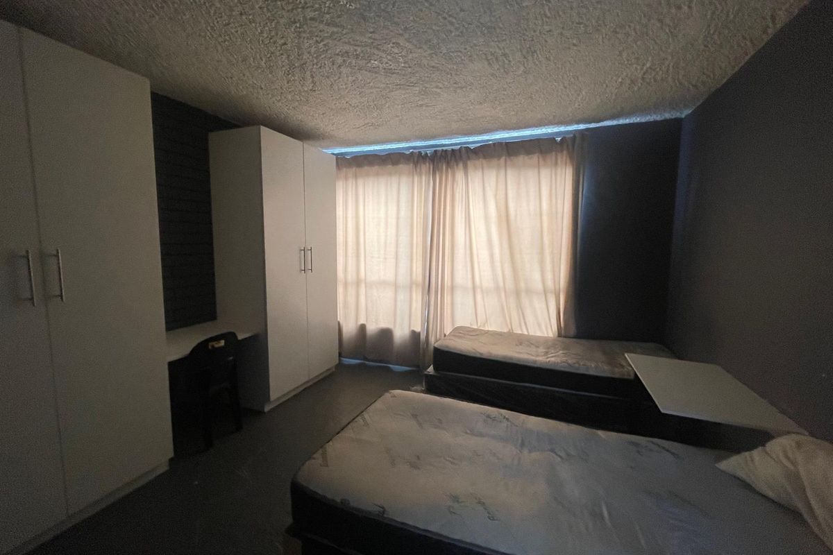 A functional bedroom featuring built-in cabinetry, a desk area, and large windows with curtains, providing a practical space for occupants.