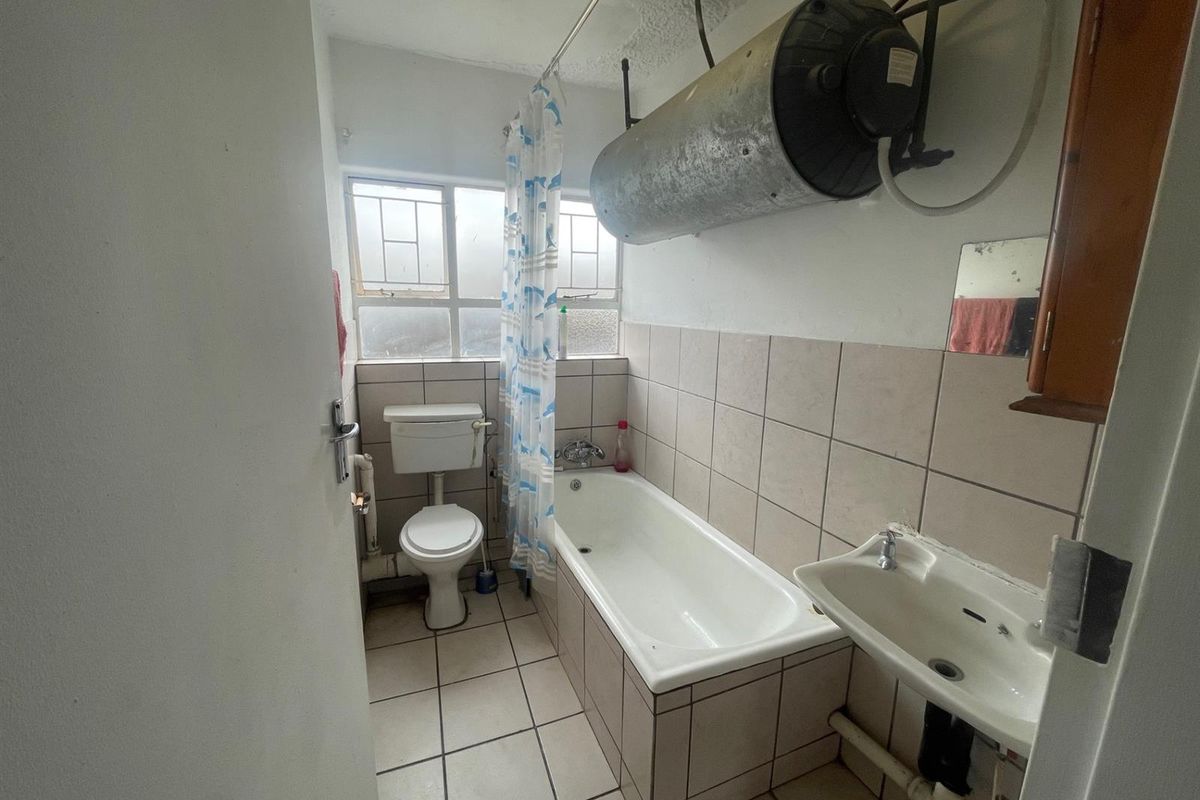 A functional bathroom featuring a bathtub, toilet, wall-mounted basin, and an exposed electric water heater unit.