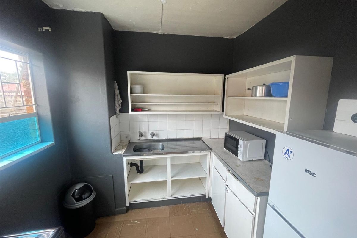 A compact kitchen area featuring basic cabinetry, a stainless steel sink, tiled splashback, and dark painted walls.