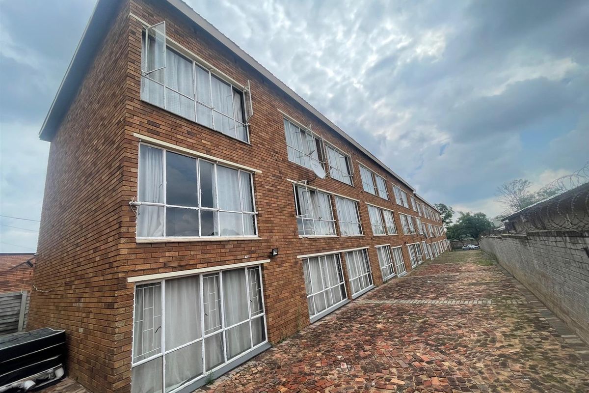 Exterior view of a multi-story commercial brick building featuring large windows and a paved side access area.