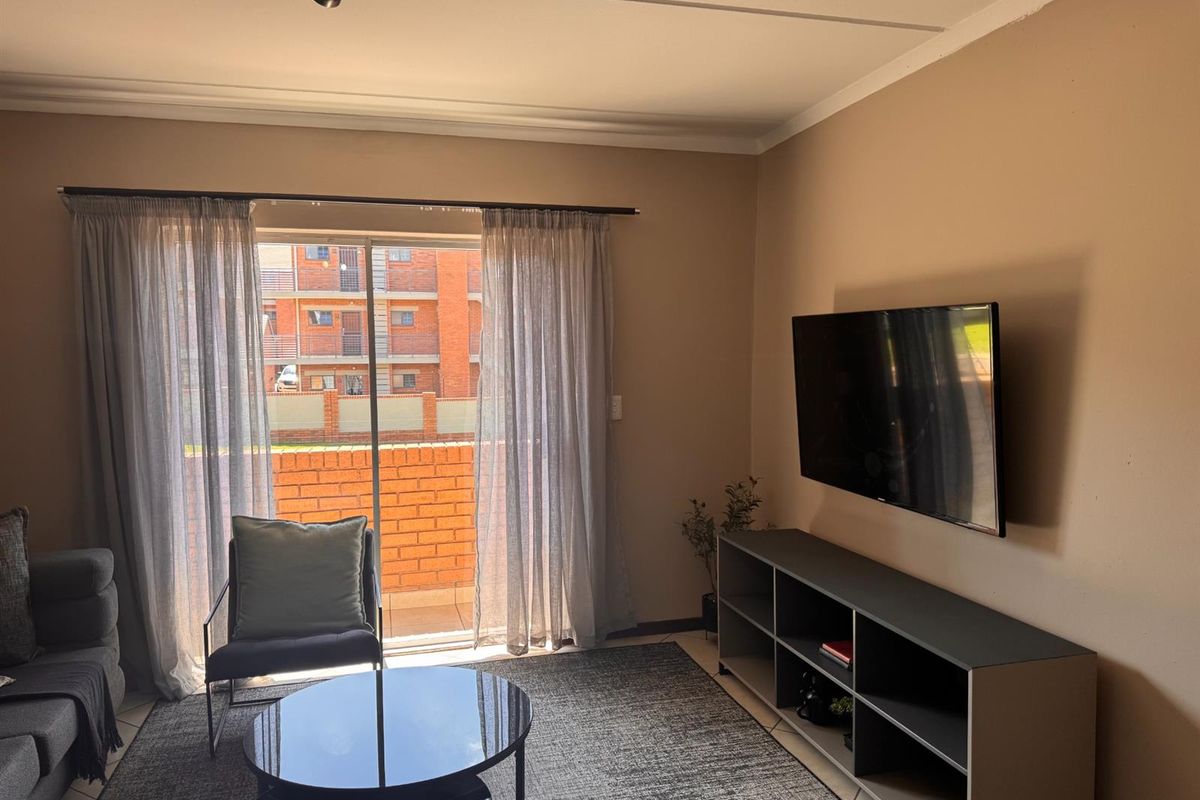A comfortable living room featuring tiled flooring, coved ceilings, and a sliding glass door that provides access to an outdoor balcony area.