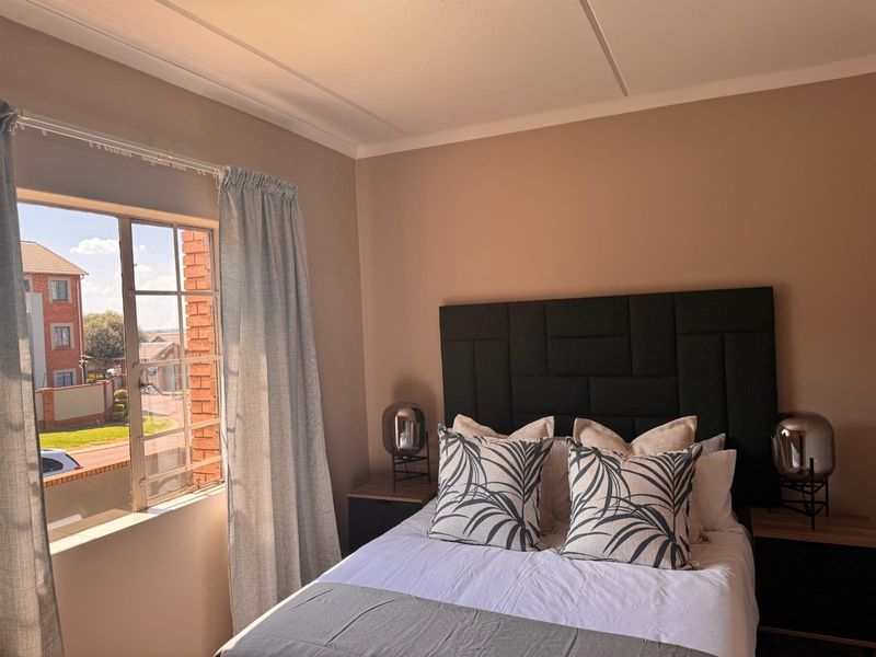 A well-lit bedroom featuring a steel-framed window with views of the surrounding complex and a neutral color palette.