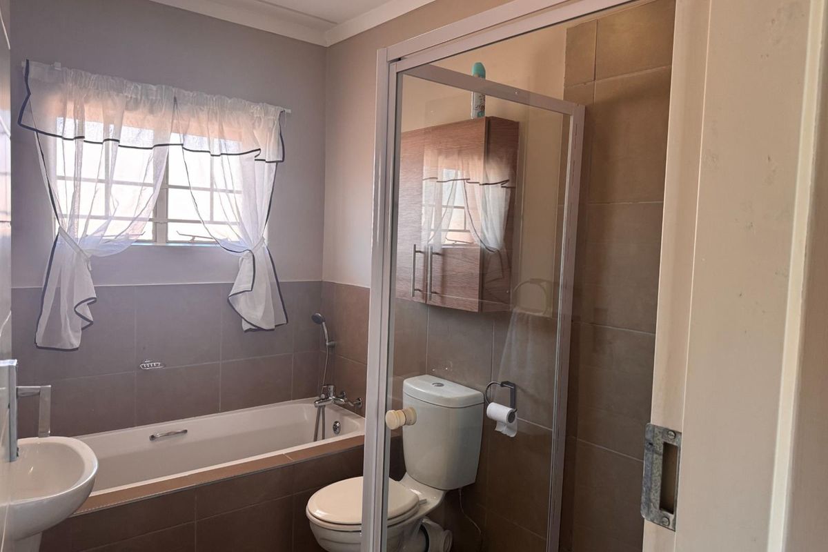 A functional bathroom featuring a bathtub, separate shower enclosure, pedestal basin, and wall-mounted storage cabinet with neutral wall tiling.