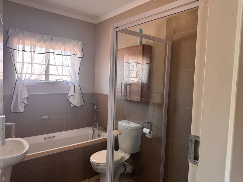 A functional bathroom featuring a bathtub, separate shower enclosure, pedestal basin, and wall-mounted storage cabinet with neutral wall tiling.