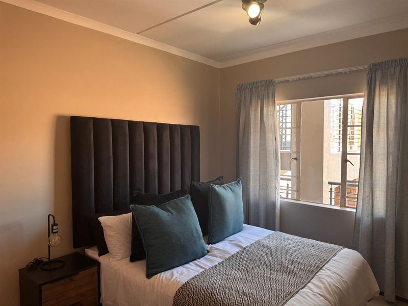 A cozy bedroom featuring a window with security bars, neutral wall tones, and a ceiling light fixture.