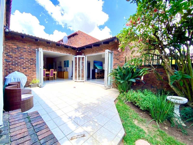 A well-maintained rear patio featuring face brick walls, tiled flooring, and folding glass doors that provide seamless indoor-outdoor flow to the garden area.