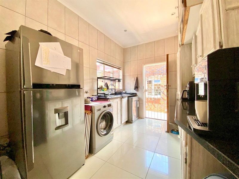 A functional scullery area featuring tiled finishes, built-in cabinetry with granite countertops, and direct access to the exterior via a security gate.