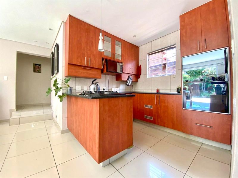A functional kitchen featuring warm-toned cabinetry, granite countertops, a gas hob, and a built-in oven, with tiled flooring throughout.