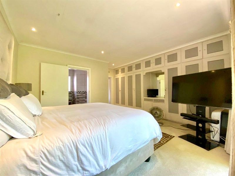 Spacious bedroom featuring extensive built-in cabinetry, recessed downlighting, and direct access to an en-suite bathroom.