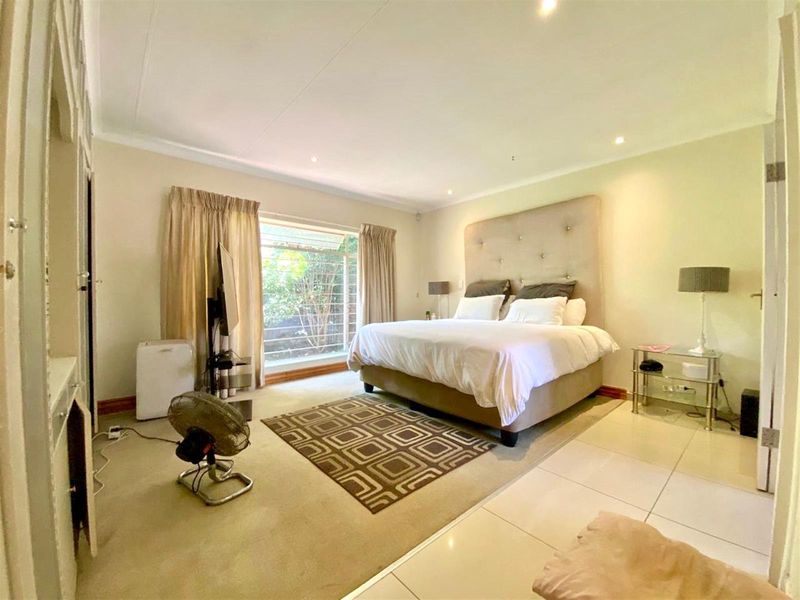 A spacious bedroom featuring a mix of tiled and carpeted flooring, built-in cupboards, and recessed downlighting, offering a comfortable and functional living space.