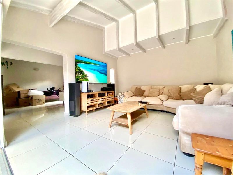 Spacious living room featuring high ceilings with exposed beams, large format floor tiles, and an open-plan layout connecting to adjacent living areas.