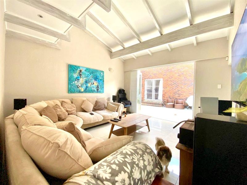 Spacious living room featuring high vaulted ceilings with exposed timber beams, large format floor tiles, and seamless access to an outdoor patio area.