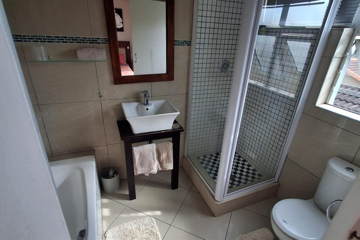 A functional bathroom featuring a vessel sink, separate shower enclosure, bathtub, and toilet with neutral wall and floor tiling.
