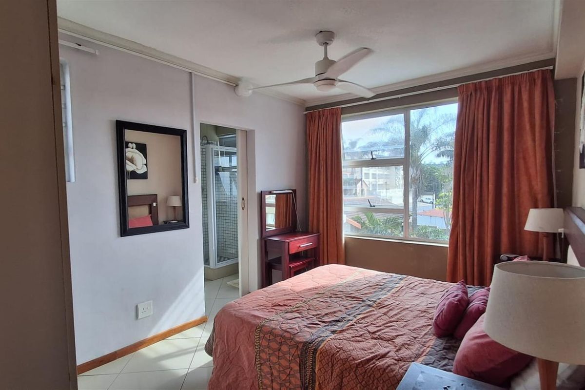 A well-lit bedroom featuring tiled flooring, a ceiling fan, and an attached en-suite bathroom with a shower.