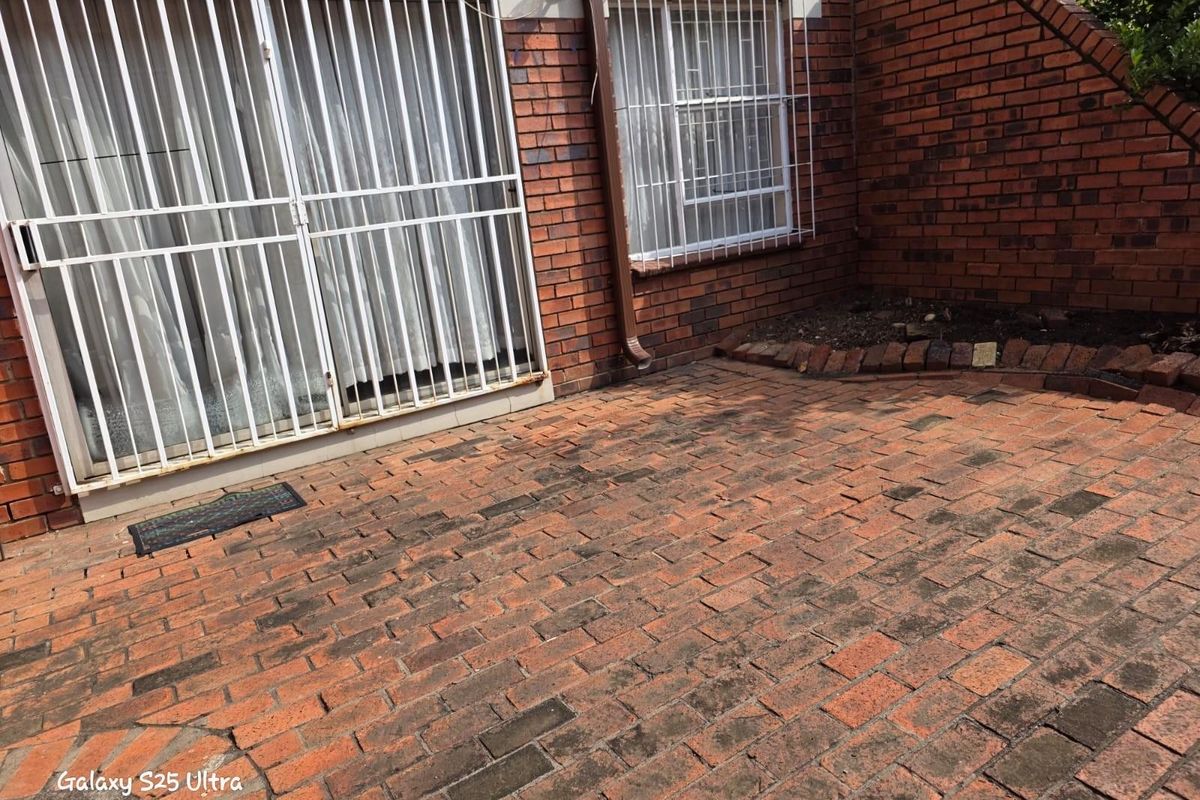 A rear patio area featuring red brick paving, exposed brick walls, and security bars on the windows and sliding door.
