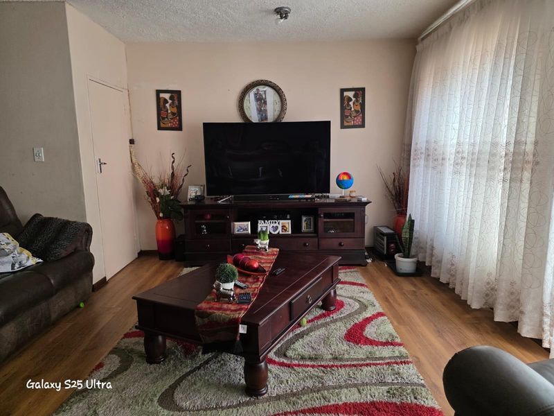 A comfortable living room featuring wood-look flooring, neutral wall tones, and large windows with sheer curtains, providing a bright and functional living space.