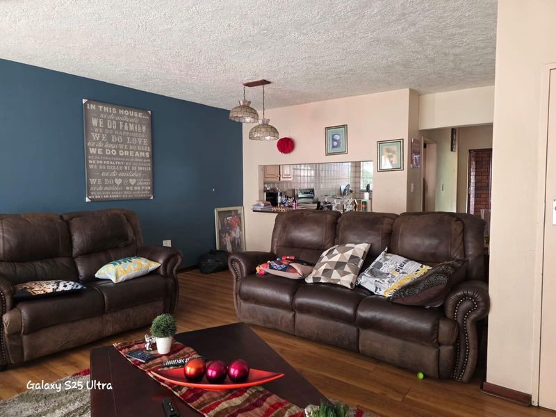 Open plan living area featuring wood-look flooring, a feature wall, and a service window connecting to the kitchen space.