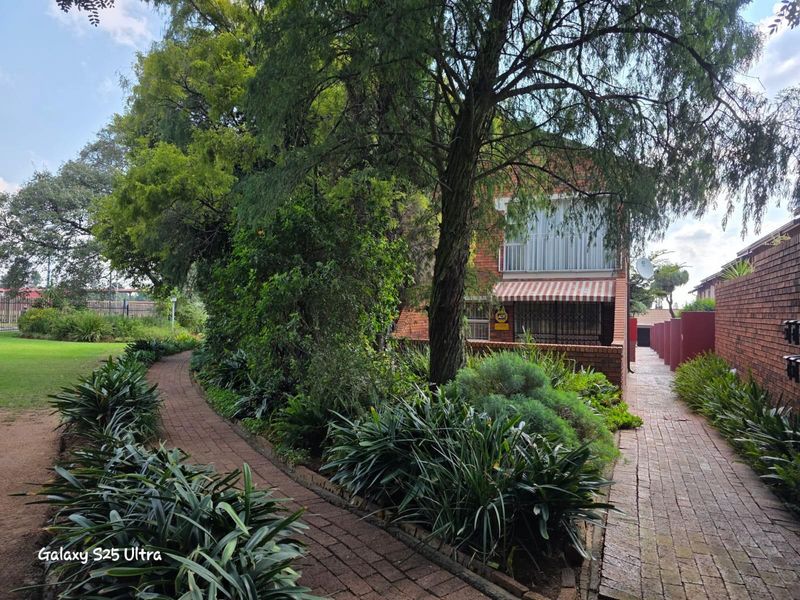A view of the property exterior featuring a brick pathway, landscaped garden beds, and mature trees leading towards the building facade.
