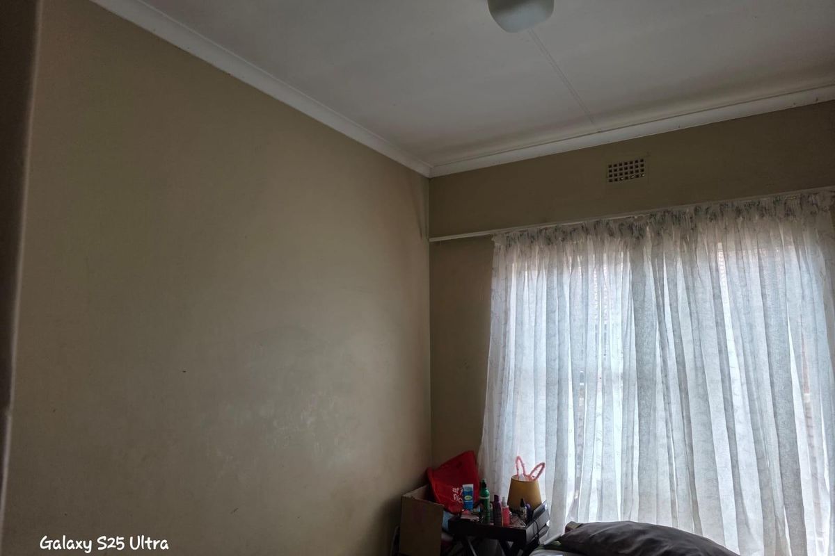A bedroom featuring a window with curtain track and ventilation vent, requiring cosmetic updates to the wall finishes.