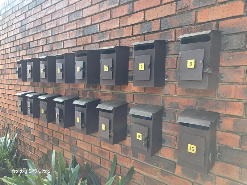 A bank of sixteen wall-mounted metal mailboxes secured to a red brick exterior wall.