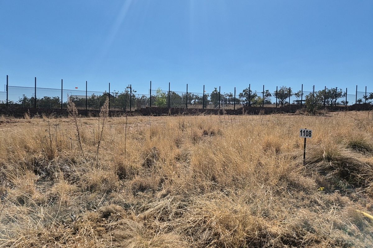 A vacant residential plot featuring dry grass, a boundary wall, and electric fencing, marked with plot number 1108.