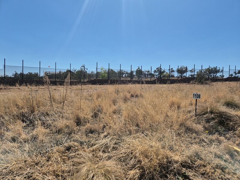 A vacant residential plot featuring dry grass, a boundary wall, and electric fencing, marked with plot number 1108.