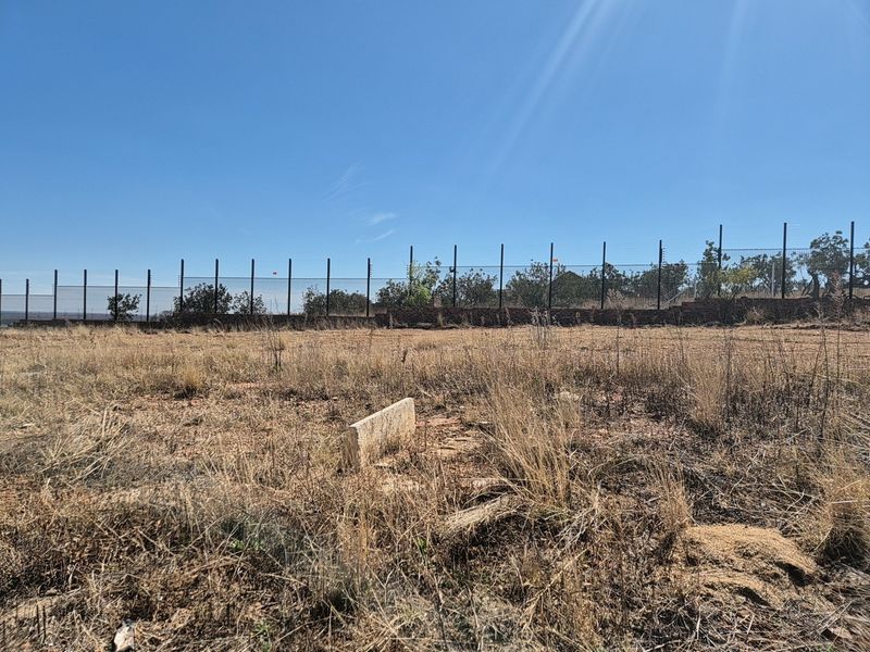 A vacant residential plot featuring dry grass, enclosed by a perimeter wall and electric fencing.