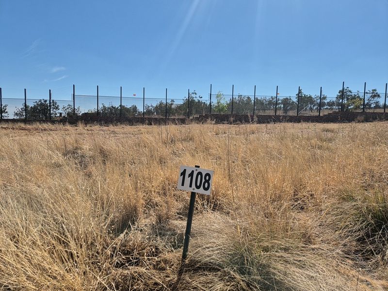 A vacant residential plot featuring dry grass, a boundary wall, and an electric fence, marked with plot number 1108.