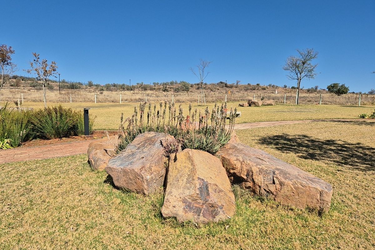 A well-maintained residential garden featuring a decorative rockery, brick pathways, and open lawn space with perimeter fencing.