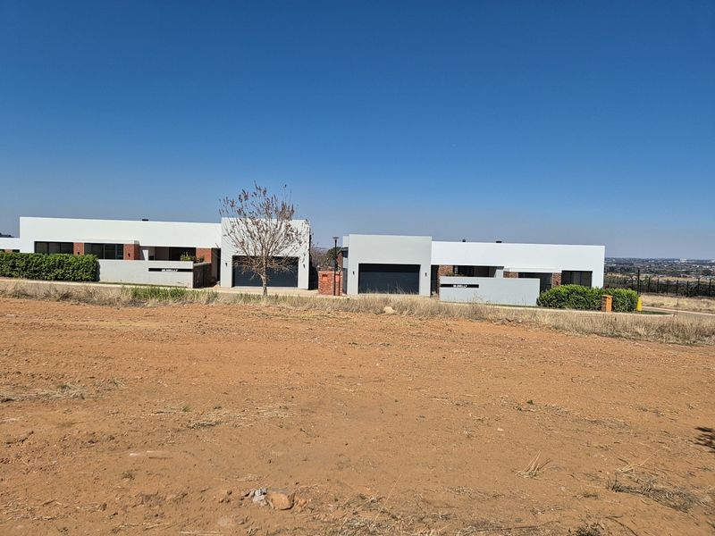 A view of modern residential properties with double garages, situated on a large, undeveloped plot of land.