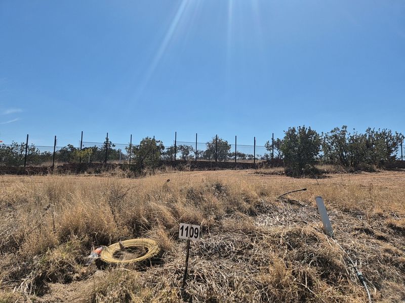 A vacant residential plot featuring dry grass, boundary wall, and electric fencing, ready for development.