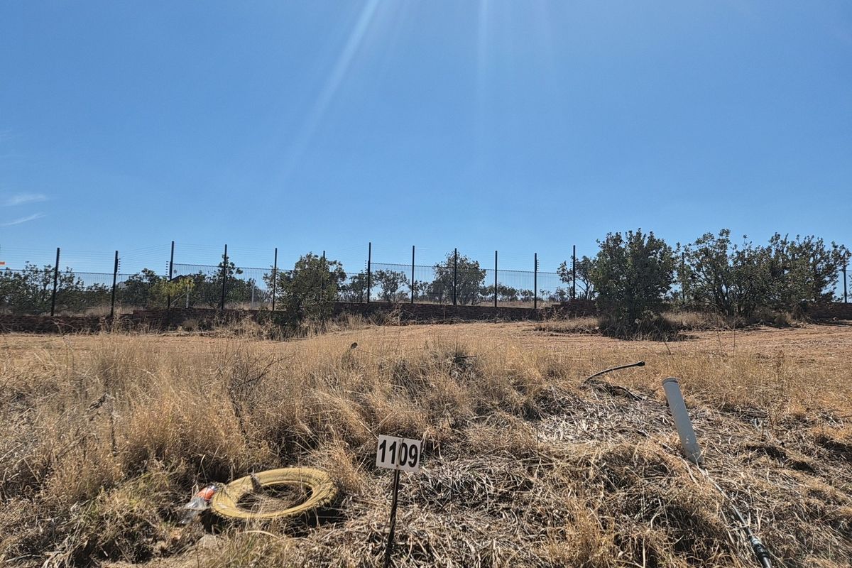 A vacant residential plot featuring dry grass, boundary wall, and electric fencing, ready for development.