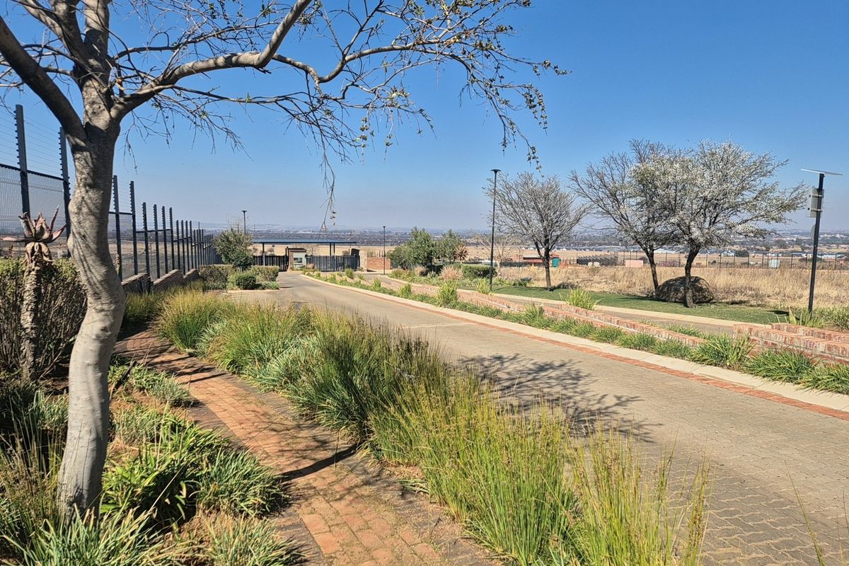 A view of a paved residential street within a secure estate, featuring manicured verges, brick edging, and perimeter electric fencing.