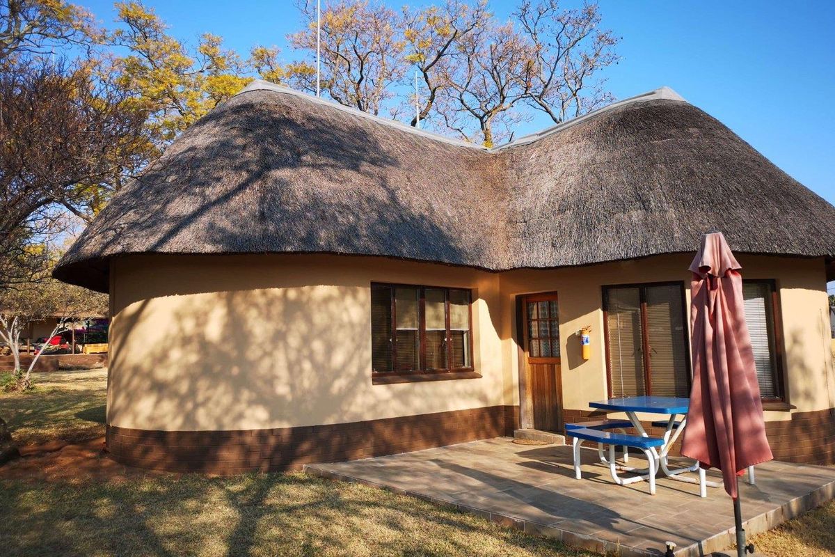 A charming thatched-roof commercial unit featuring a paved patio area, timber-framed windows, and a wooden entrance door set within a landscaped garden.