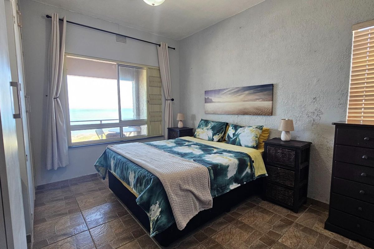 A bedroom featuring tiled flooring, a built-in wardrobe, and a large window offering ocean views, providing a bright and airy atmosphere.