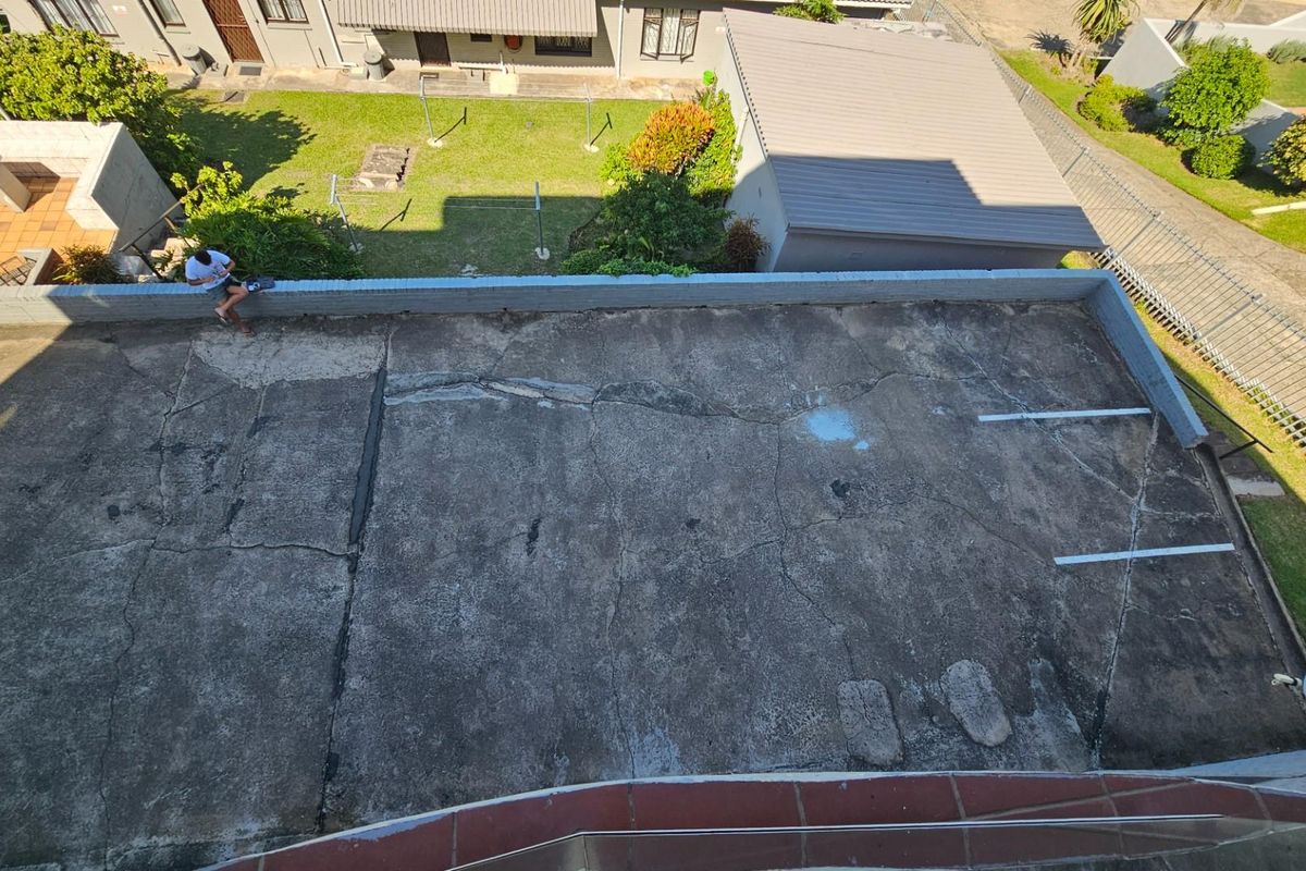 An elevated view of a concrete parking area showing significant surface cracking and signs of wear, located within an apartment complex.