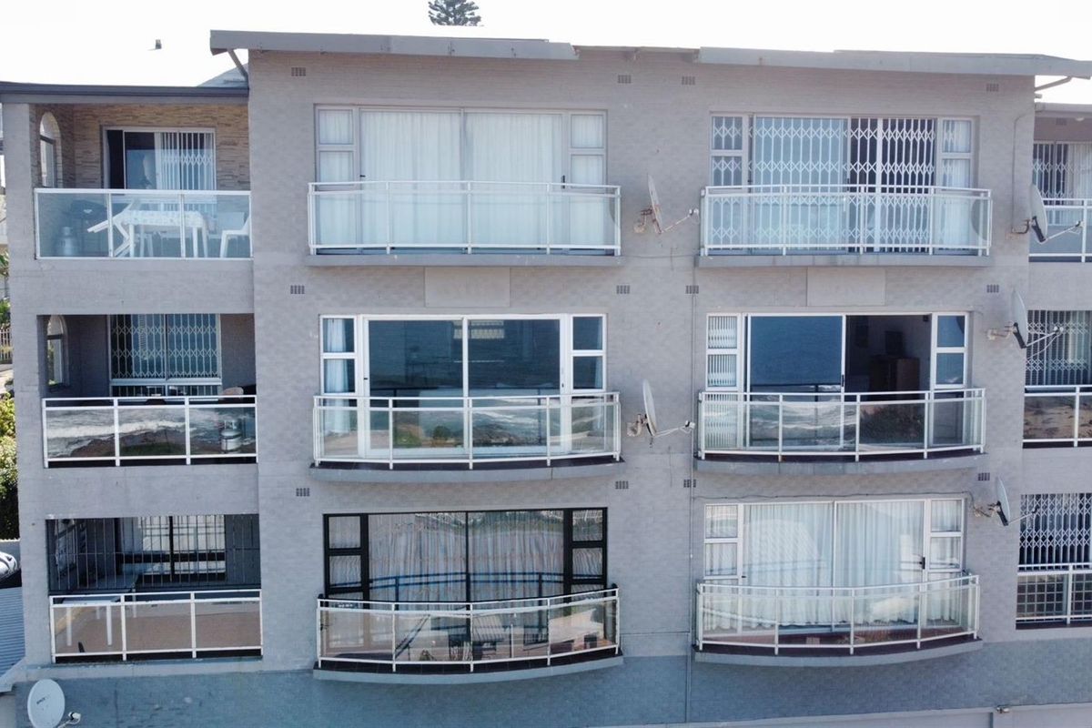 Exterior view of a multi-story apartment building featuring private balconies with glass railings and security gates.
