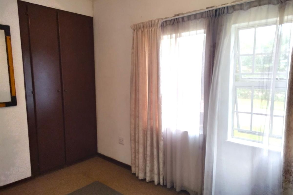 A bedroom featuring built-in cupboards, carpeted flooring, and a window with natural light.