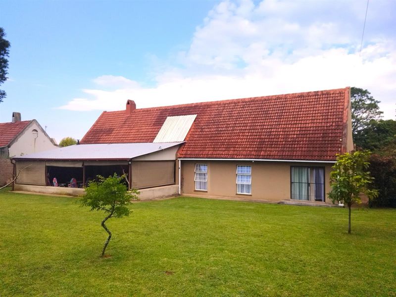 Rear view of the property featuring a large lawn, a covered patio area, and a pitched tiled roof with a section of replacement roofing.