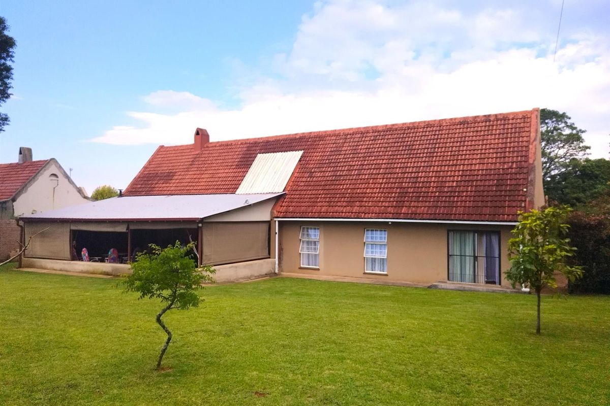 Rear view of the property featuring a large lawn, a covered patio area, and a pitched tiled roof with a section of replacement roofing.