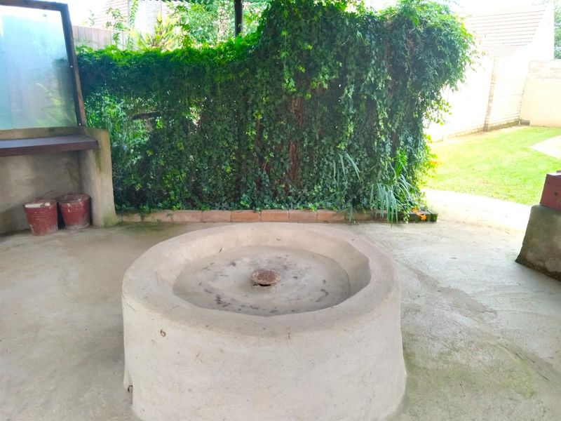 Outdoor patio area featuring a built-in concrete fire pit or braai structure, set against a lush ivy-covered boundary wall.