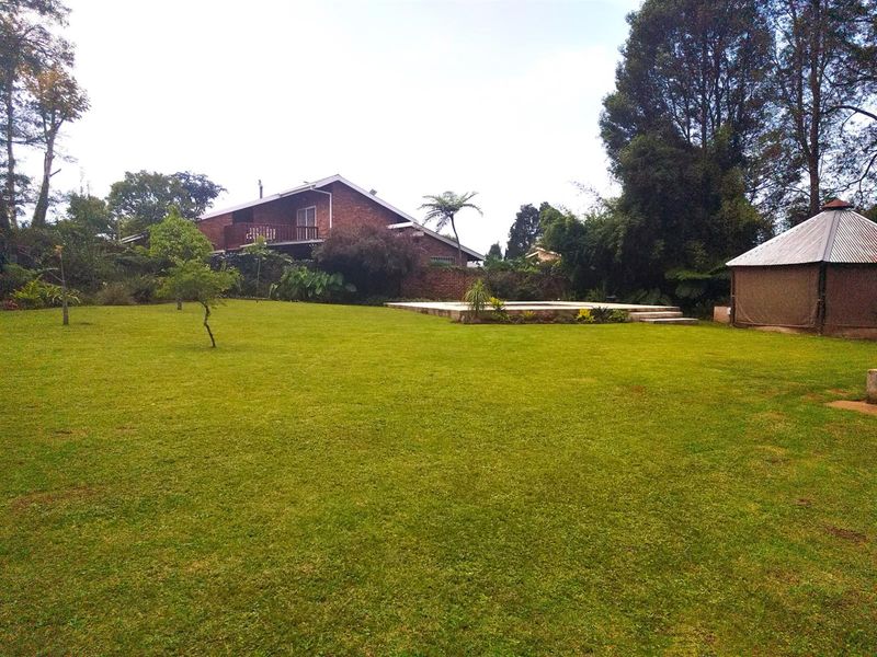 Spacious rear garden featuring a large lawn, a swimming pool area, and a detached outdoor structure, set against the backdrop of the main house.